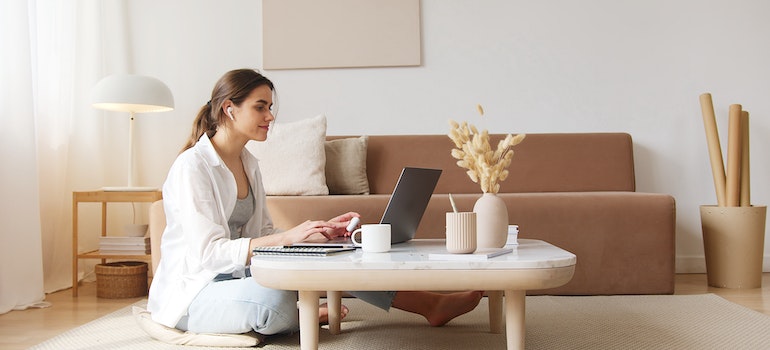 A woman sitting on the floor in a white beige living room looking at her laptop and trying to find a job before moving from Orlando to Lakeland