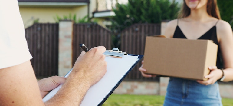 A woman standing with a cardboard box in front of a man with a notepad in his hands working with local movers Sunny Isles Beach