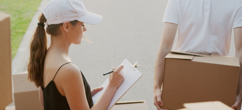 A woman doing a checklist, while a man is holding a moving box