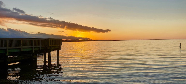 a dock over calm waters with an orange sunset