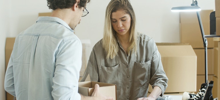two people talking while packing things in cardboard boxes