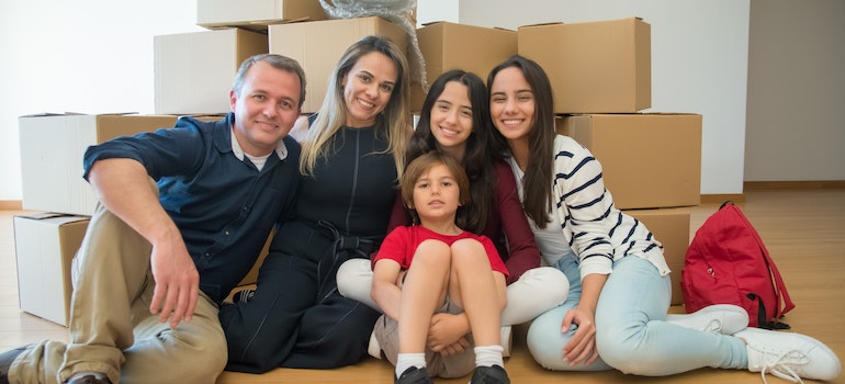a family of five sitting on hardwood floors in front of packed moving boxes waiting for residential movers Sunny Isles Beach