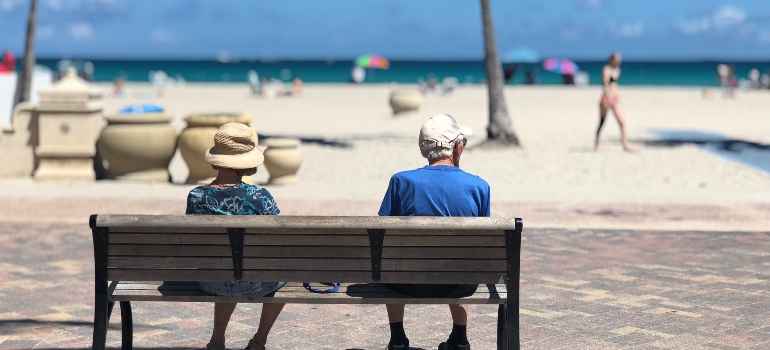 A man and a woman sitting on a bench near a beach
