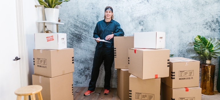 A man who is working for long distance movers North Fort Myers standing surrounded by moving boxes