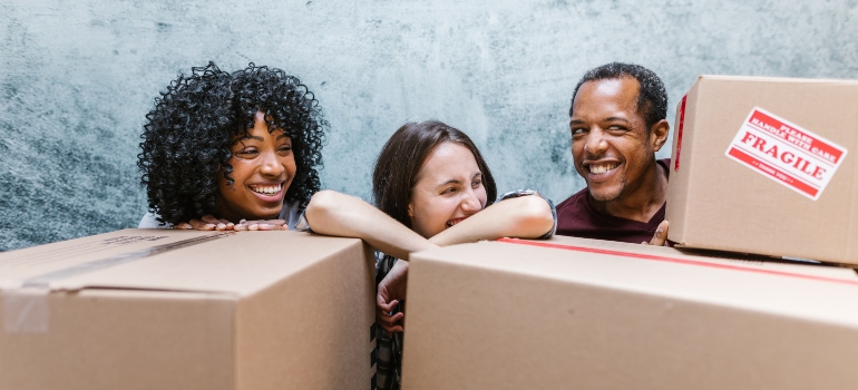 Two women and a man smiling behind moving boxes 