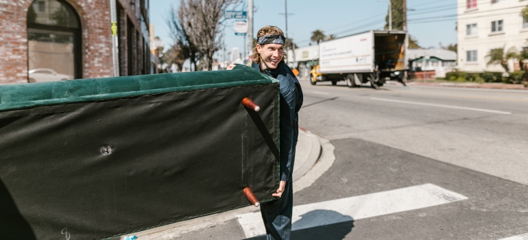 A man carrying a green velvet couch while crossing the street