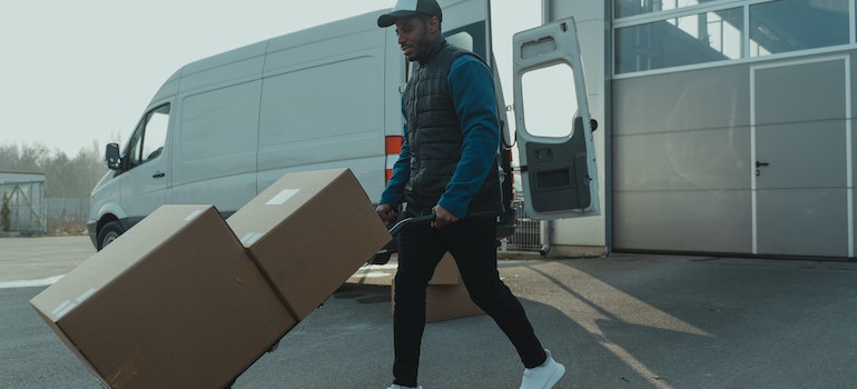A mover carrying moving boxes with a dolly next to a moving van