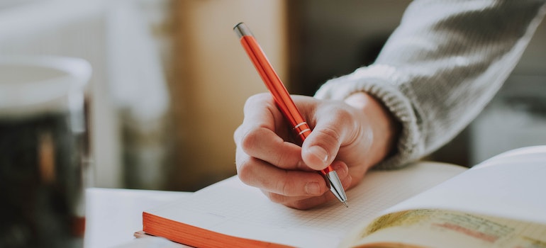 A person writing a list of tips to help them when moving from Lakeland to Miami with an orange pen