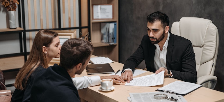 a man talking to his clients pointing at a document while sitting in a beige leather chair