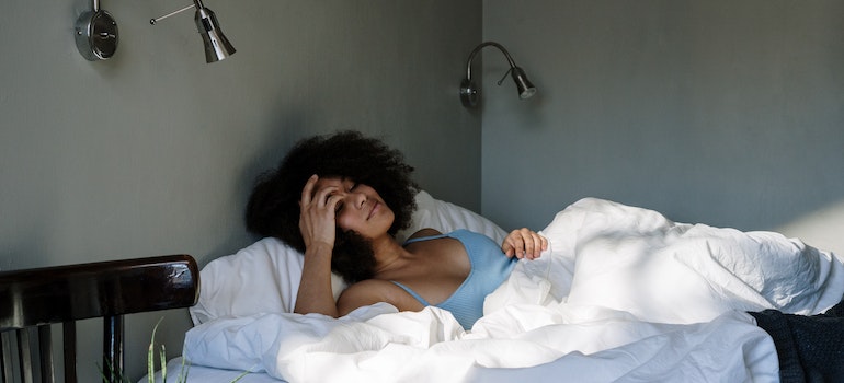 Woman lying in her bed under white sheet while doing self-care when moving