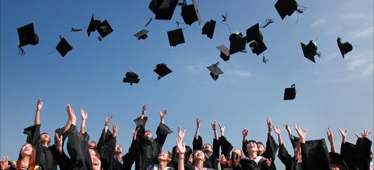 Newly graduated people wearing black academy gowns and throwing hats up in the air