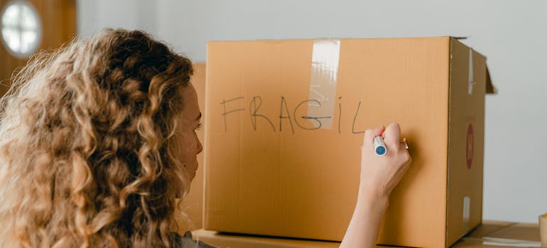 a woman writing Fragile on a cardboard box
