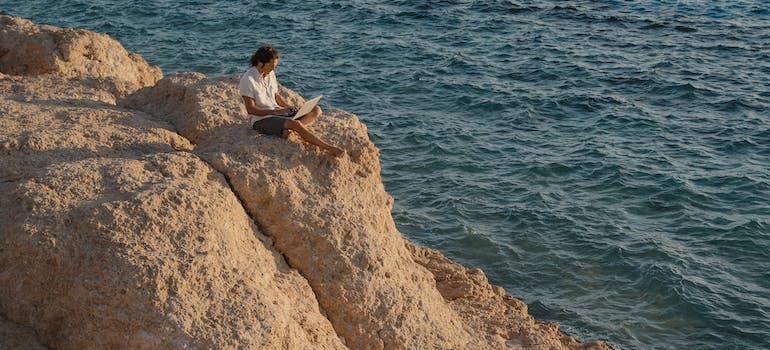 a man sitting on a rock and reading on a laptop about moving from Tampa to Pompano Beach