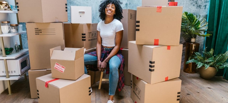 A woman sitting on a chair among boxes and thinking about what packing supplies should you use