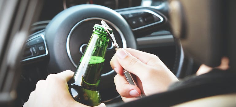 A person opening a beer bottle in the car
