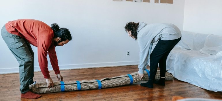 A couple trying to pack a carpet for a Boynton Beach move